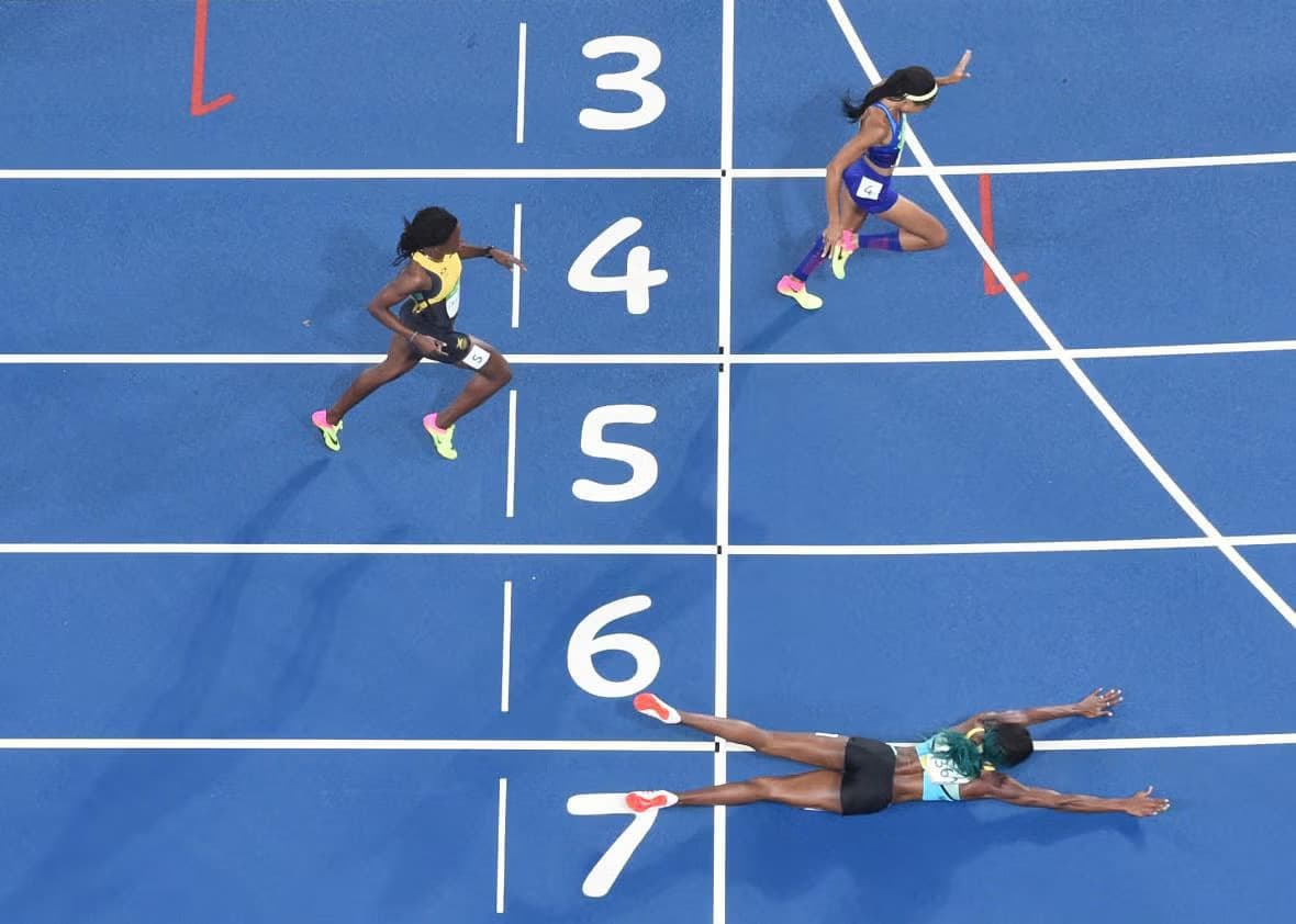 Sprinters crossing the finish line of a track race, one diving across the line.