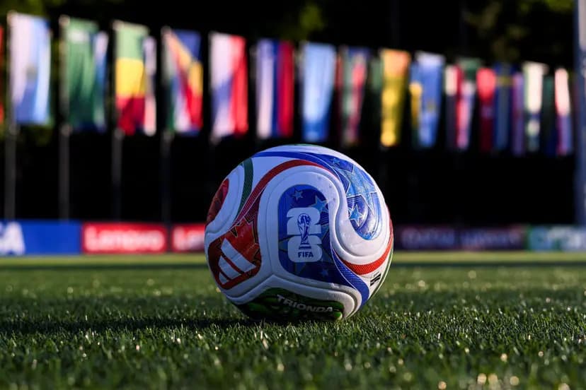 The official FIFA World Cup 2026 Trionda ball resting on grass with international flags blurred in the background.