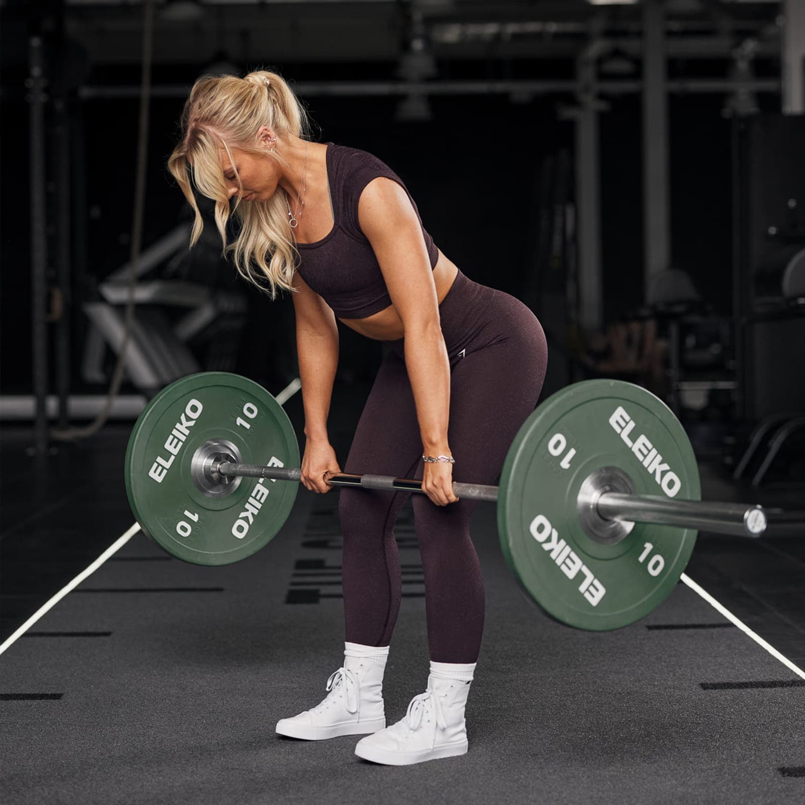 A woman performing a barbell deadlift in a gym, the lift most associated with low-back loading.