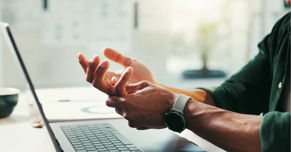 A person at a laptop shaking out and holding their tingling wrist and hand after long desk work.