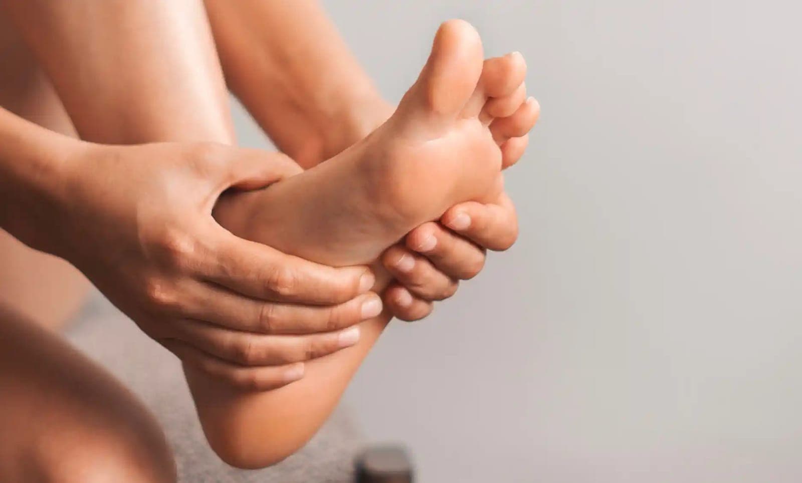 Close-up of a person holding and massaging the sole and heel of their bare foot.