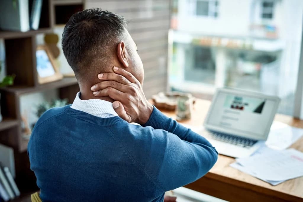 A man at his desk rubbing the back of his neck, a classic posture associated with tech neck.